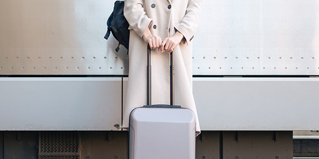 Una chica espera el tren con su maleta a punto de viajar